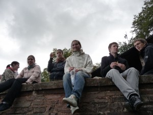 Sechs Personen sitzen auf einer Mauer, blicken auf Fotografen herab