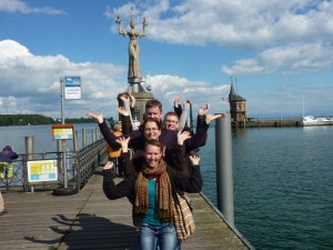 Sechs Personen hintereinander, Imperia-Statue in Kontanz imitierend, sehen aus wie vielarmige indische Gottheit