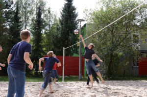Fünf Personen auf Volleyballfeld, Mann schmettert Volleyball über das Netz