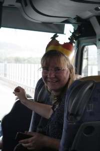 Frau mit Papierkrone in Deutschlandfarben im Reisebus, sich im Sitz halb umdrehend und lachend