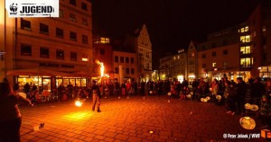 Eine Person macht Feuershow, rundherum viele Menschen mit Lampions, im Hintergrund Häuser